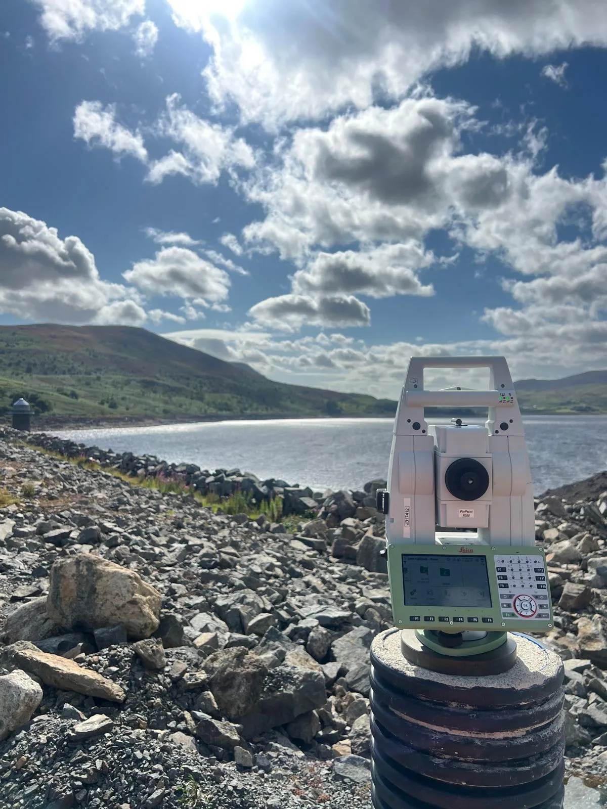 Robotic total station on a survey pillar above a reservoir, with hills beyond